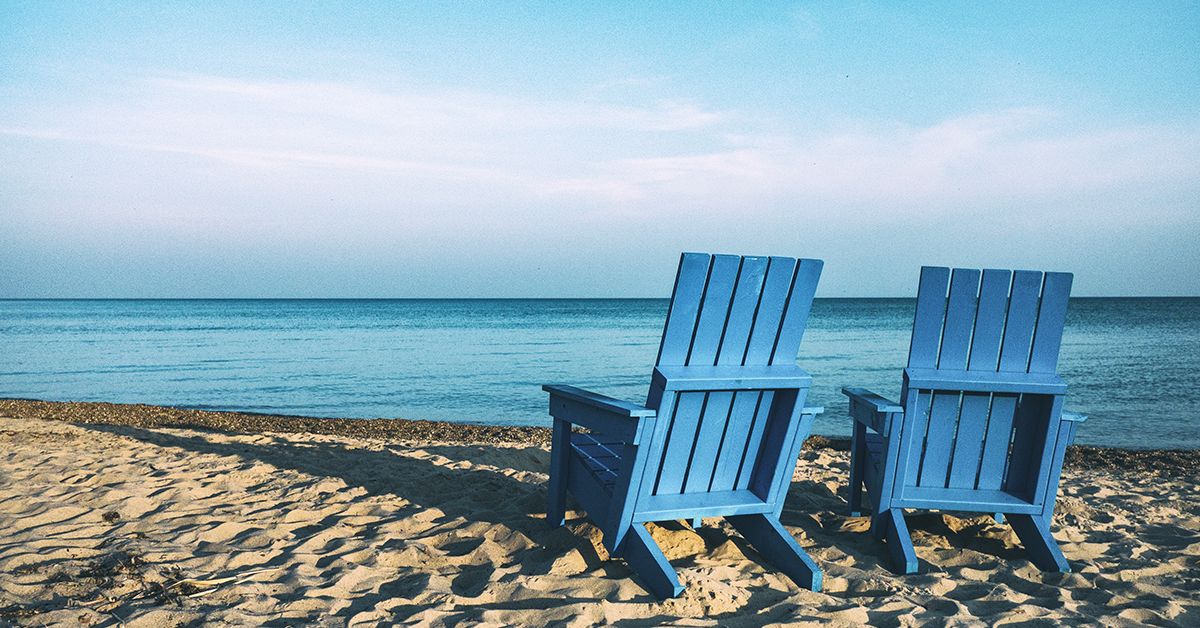 Two blue lounge chairs on abeach facing the water