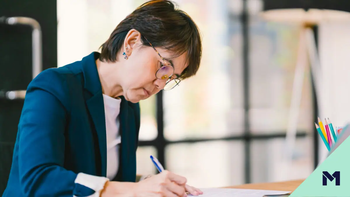 Mature woman managing finances in a notebook while sitting at a desk