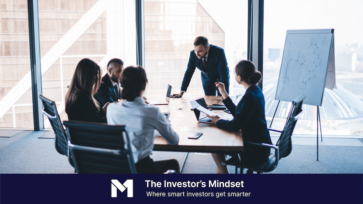 Five business people sitting around a conference table with a whiteboard easel in the background