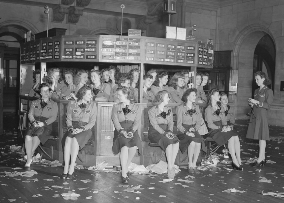 Around 20 women standing and sitting around the hub of the New York Stock Exchange in black/white color.