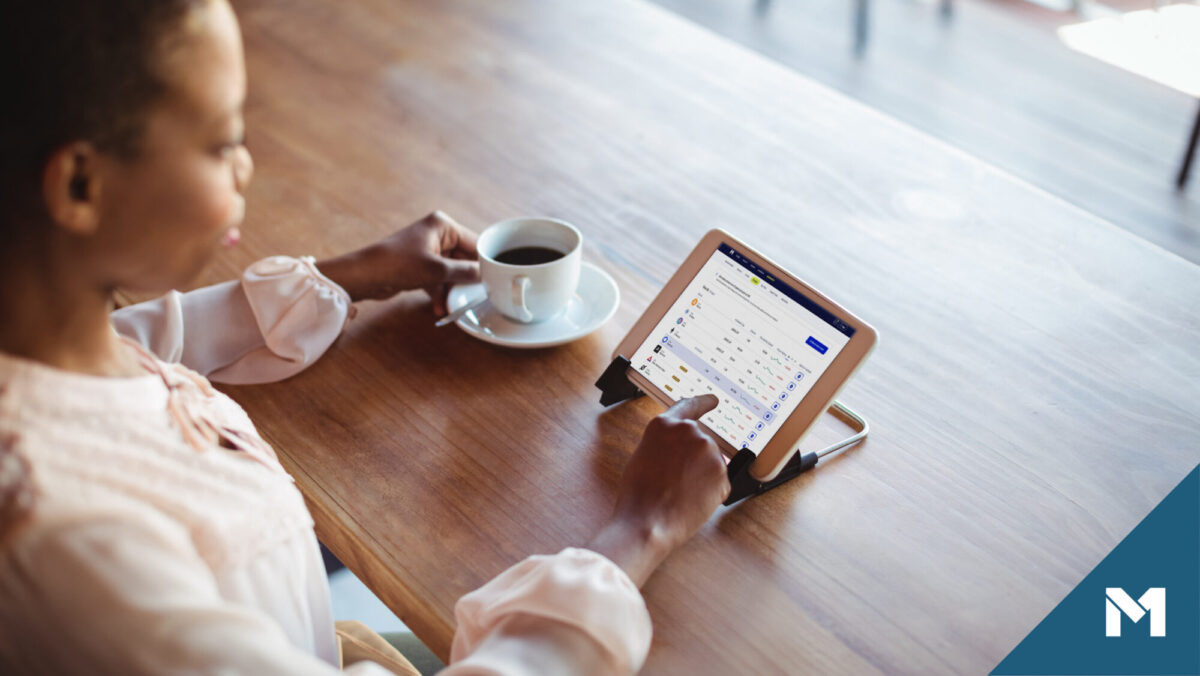 Woman sitting at wood table using a tablet with M1 Crypto research page on the screen