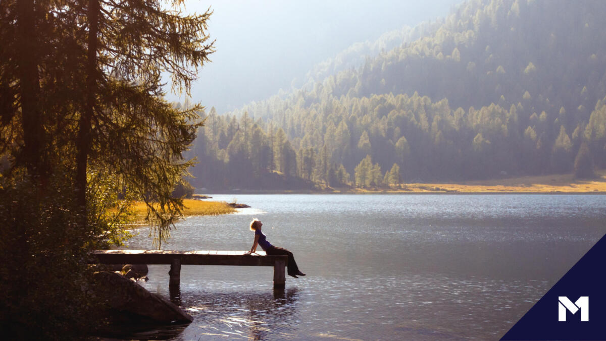 Woman relaxing on a dock overlooking a lake, surrounded by tress