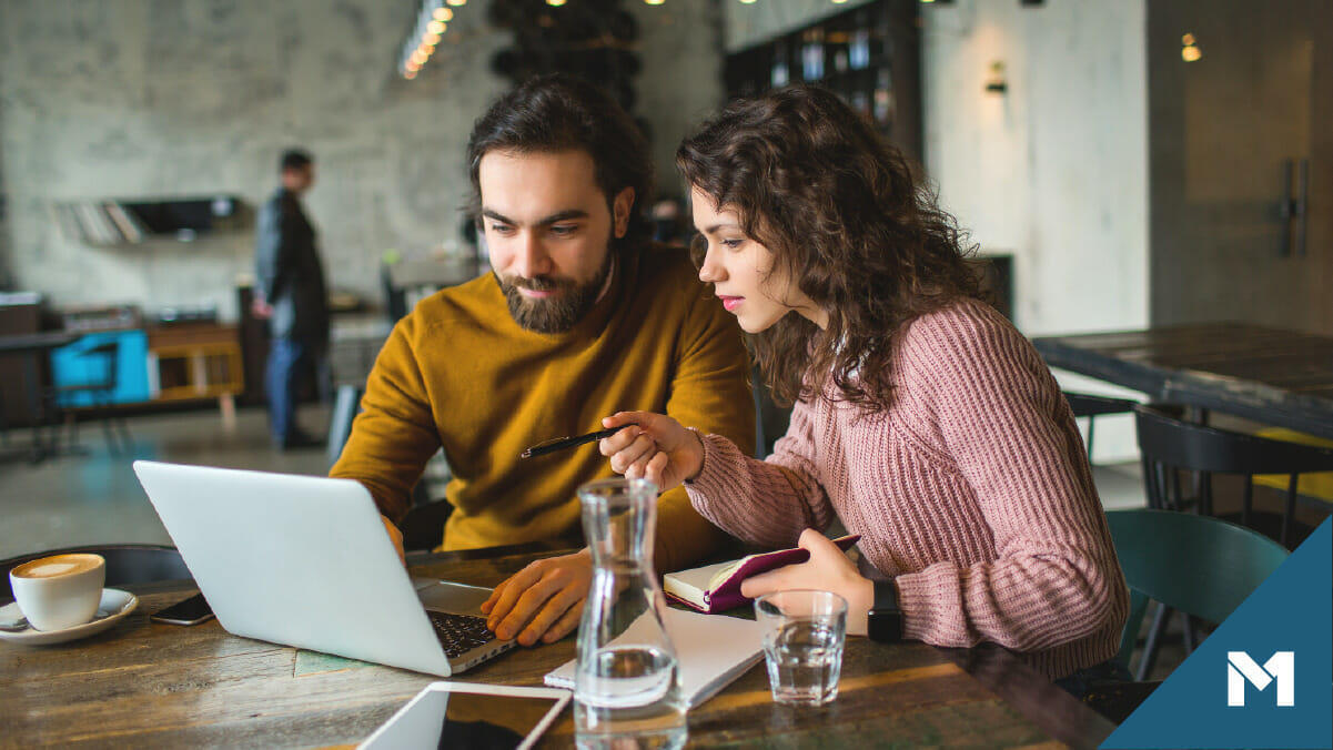 Man and woman managing finances together on laptop computer in a cafe