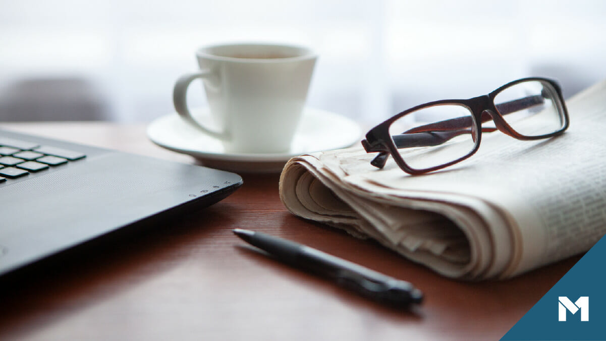 Desktop of investor with newspaper, glasses, coffee, and a laptop