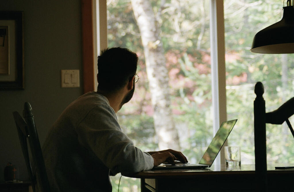 Man taking a break from reviewing finances on laptop computer to look at nature outside the window