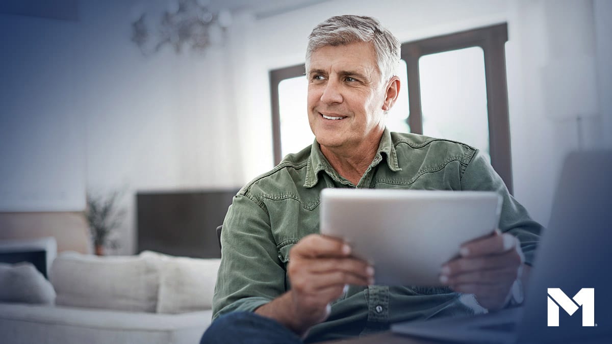 Gray-haired man reading something on his tablet in his living room and looking optimistic.